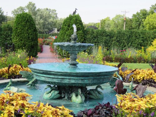 A decorative fountain surrounded by vibrant flowers and lush greenery in a serene garden setting.