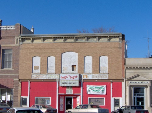A brick building with a red facade, featuring signs for a saloon and lottery, under a clear blue sky.