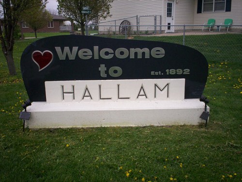 Welcome sign for Hallam, established in 1892, surrounded by grass and trees.