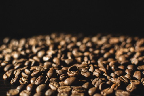 Close-up of scattered coffee beans on a dark surface, showcasing their rich texture and color.