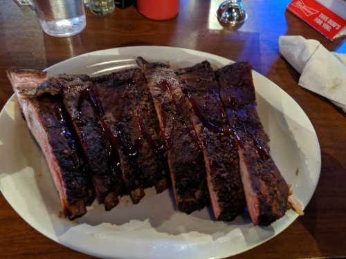 A plate of smoked ribs drizzled with barbecue sauce, served on a wooden table.