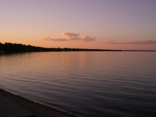 A serene lake at sunset, with calm waters reflecting soft pink and orange hues in the sky.