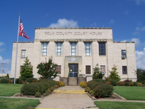 Front view of the Polk County Courthouse, featuring a flag, landscaped grounds, and a clear blue sky.