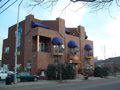 A modern brick building with blue awnings, balconies, and an American flag, set against a cloudy sky.