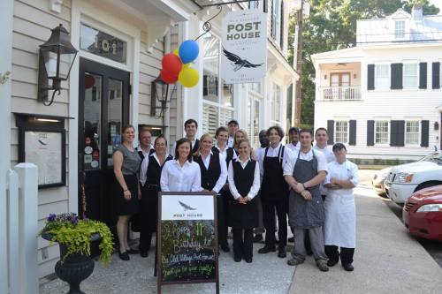 A group of staff members stands outside the Post House restaurant, smiling, with balloons and a sign celebrating a birthday.