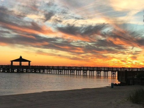 A serene sunset over a pier, with vibrant clouds reflecting on calm waters.