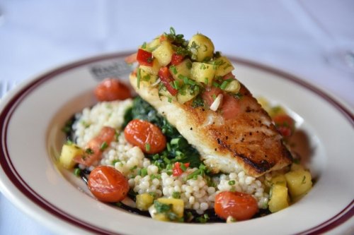 Grilled fish topped with fresh salsa, served on a bed of couscous and spinach, garnished with cherry tomatoes.