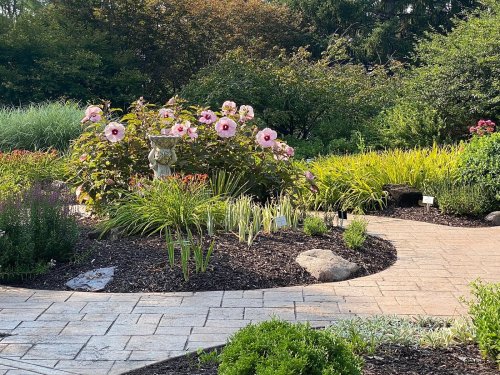 A garden path winding through vibrant flowers and lush greenery, featuring a stone statue among the plants.