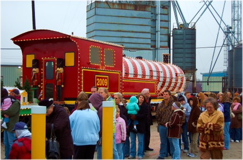 A festive red train with a striped caboose, surrounded by a crowd of people in winter clothing.