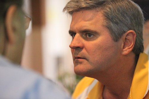 A man in a yellow shirt intensely engages in conversation with another person.