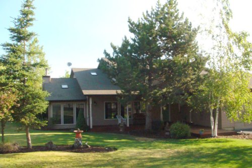 A spacious house surrounded by trees and a well-maintained lawn on a sunny day.