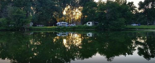 A serene river scene with trees and campers reflected in the calm water at sunset.
