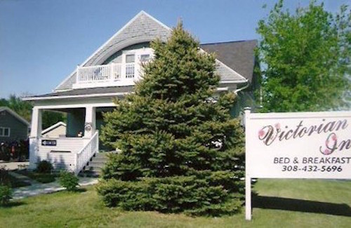 A charming Victorian-style bed and breakfast with a large tree in front and a welcoming sign.