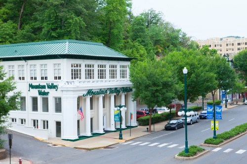 Historic building with green accents, labeled "Mountain Valley Water," surrounded by trees and parked cars.