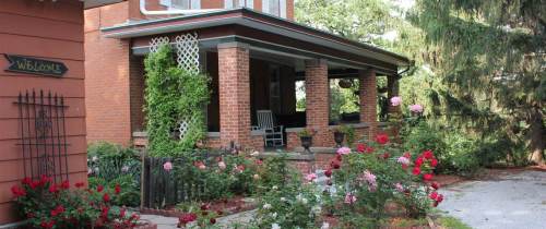 A charming brick house with a porch, surrounded by colorful rose bushes and greenery.