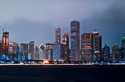 Chicago skyline at night, featuring illuminated skyscrapers and a calm waterfront.