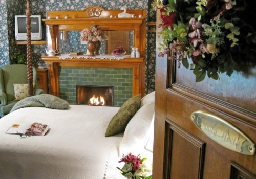 Cozy bedroom with a fireplace, floral wallpaper, and wooden decor, featuring a bed and a welcoming door.