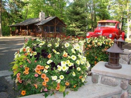 A rustic cabin surrounded by vibrant flower beds and a vintage red truck parked nearby.