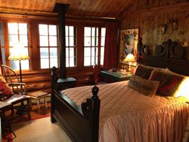 Cozy log cabin bedroom with a wooden bed, warm lighting, and large windows showcasing a rustic interior.