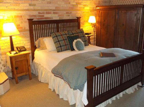 Cozy bedroom with a wooden bed, plaid pillows, warm lighting, and a vintage wardrobe against a brick wall.