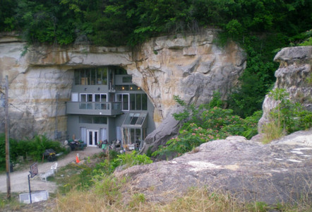 A modern house built into a rocky cliff, surrounded by greenery and featuring large windows.