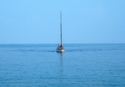 A small sailboat glides across a calm, blue sea under a clear sky.