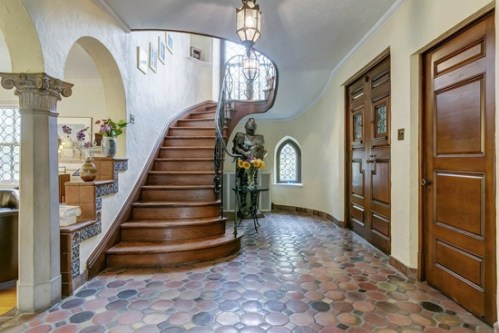 A spacious entryway featuring a curved staircase, decorative tile floor, and a statue beside wooden doors.