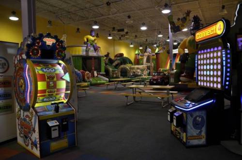 A colorful indoor play area featuring arcade games, inflatable structures, and picnic tables.
