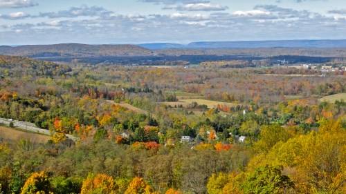 A scenic view of rolling hills and valleys adorned with vibrant autumn foliage under a cloudy sky.