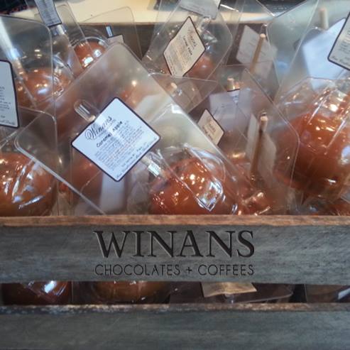 A wooden crate filled with packaged chocolates and coffees from Winans, featuring clear plastic wrapping and labels.