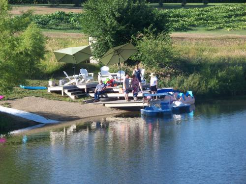 A group of people enjoying a sunny day by a dock near a calm lake, with umbrellas and lounge chairs nearby.
