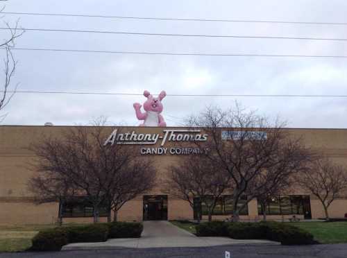 A large pink bunny figure atop the Anthony-Thomas Candy Company building, surrounded by bare trees and cloudy skies.