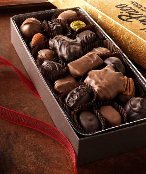 A box of assorted chocolates, featuring various shapes and fillings, arranged neatly with a red ribbon.