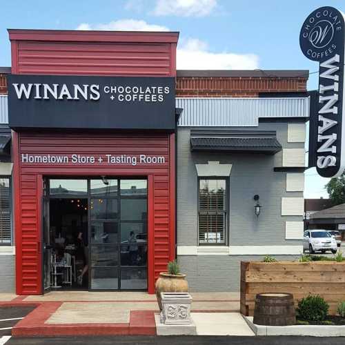 Exterior of Winans Chocolates & Coffees, featuring a red entrance and sign, with outdoor seating and a welcoming atmosphere.