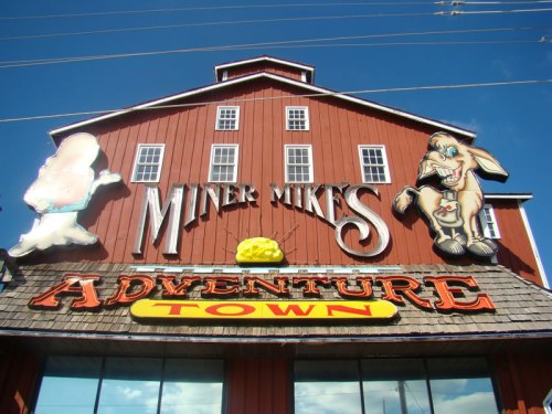 Colorful sign for "Miner Mike's Adventure Town" featuring cartoon characters on a red barn-like building.