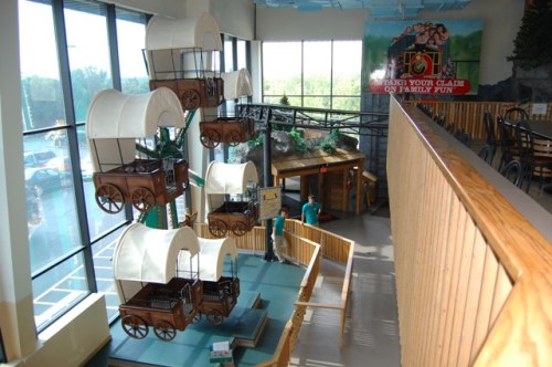 Interior view of a family entertainment center featuring large wagon structures and a wooden railing overlooking the area.