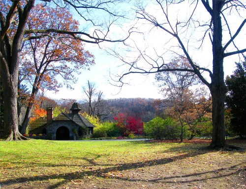 A stone cottage surrounded by colorful autumn trees and a clear blue sky in a serene landscape.