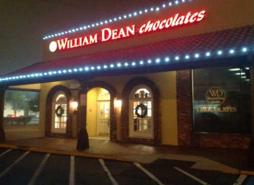 Exterior of William Dean Chocolates shop, featuring festive wreaths and illuminated signage.