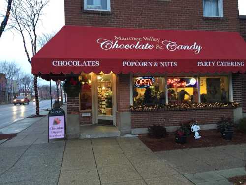 A cozy candy shop with a red awning, displaying chocolates and treats, with an "Open" sign in the window.