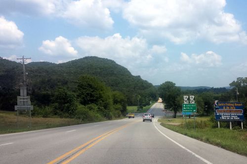 A scenic highway with mountains in the background, featuring road signs for nearby attractions and a clear blue sky.