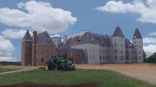 A large, unfinished castle-like structure with a tractor in the foreground, set against a blue sky with clouds.