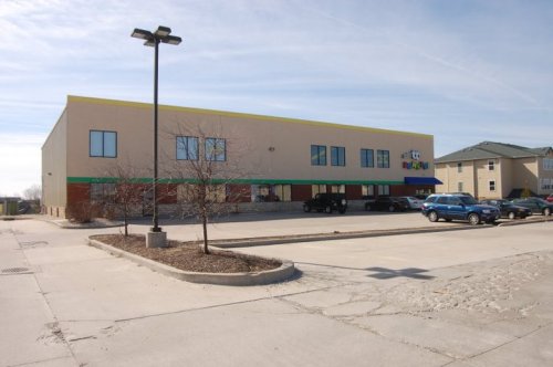 A large commercial building with multiple windows, surrounded by a parking lot and a few trees.