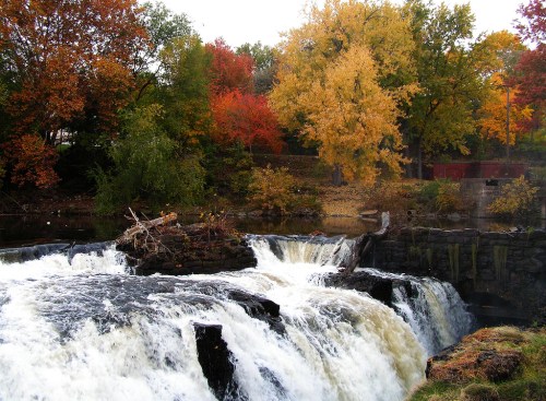 A waterfall cascades over rocks, surrounded by vibrant autumn foliage in shades of red, orange, and yellow.