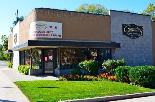 A storefront with a sign for Cummings Chocolates, featuring colorful flowers and a clear blue sky.