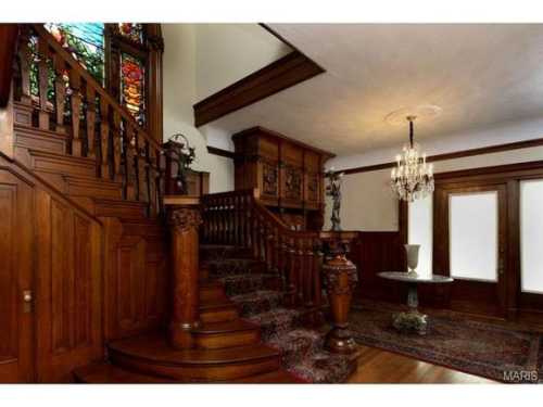 Elegant wooden staircase in a vintage foyer with stained glass windows and ornate furnishings.