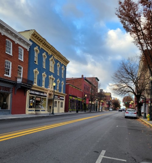 A quiet street lined with colorful buildings and trees, under a partly cloudy sky.
