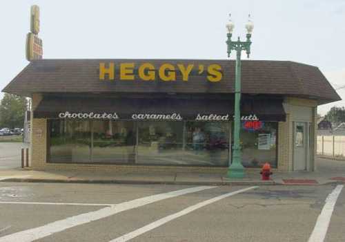 A storefront with a brown roof and large sign reading "Heggy's," featuring windows displaying chocolates and caramels.