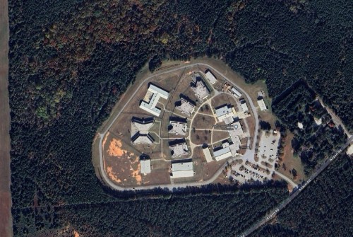Aerial view of a complex surrounded by trees, featuring multiple buildings and a parking area.