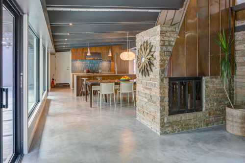 Modern interior featuring a stone fireplace, dining area, and large windows with natural light.