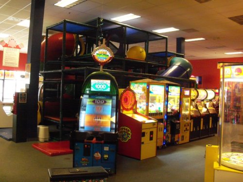 A colorful indoor play area with a multi-level structure, arcade games, and bright machines in a spacious setting.